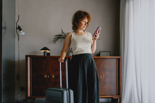 istock Woman with Suitcase Checking Phone in Modern Hotel Room 2165024747