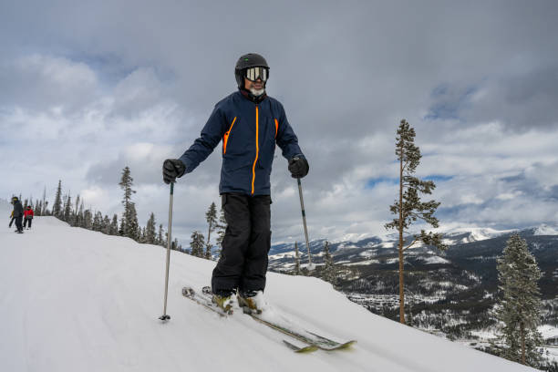 An African-American man in his fifties wearing a helmet and goggles posing on his skis with spectacular scenery behind him at a ski resort in Winter Park, Colorado.