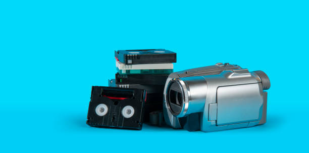 istock old video camera next to a black mini DV cassette tower on a blue surface against blue background 2165025321