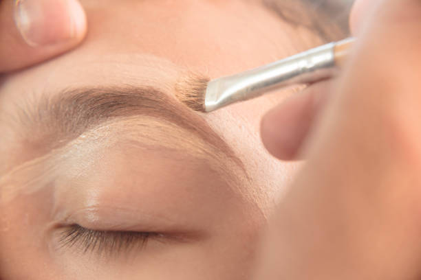 istock A makeup artist adding concealer on the top of a young woman's eyebrows with a thin angled brush. Shaping technique and avoiding plucking. 2165026346