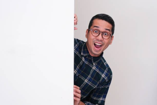 istock A man peeking from behind blank billboard showing amazed expression 2165034996