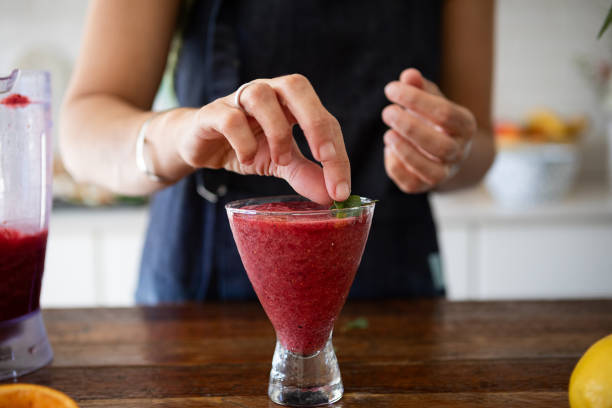 A woman's hands decorating a berry smoothie with mint leaves