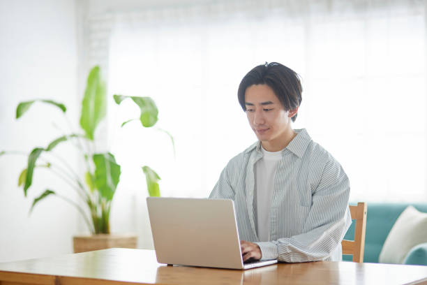 istock Male Japanese college student using a computer in the living room 2165054799