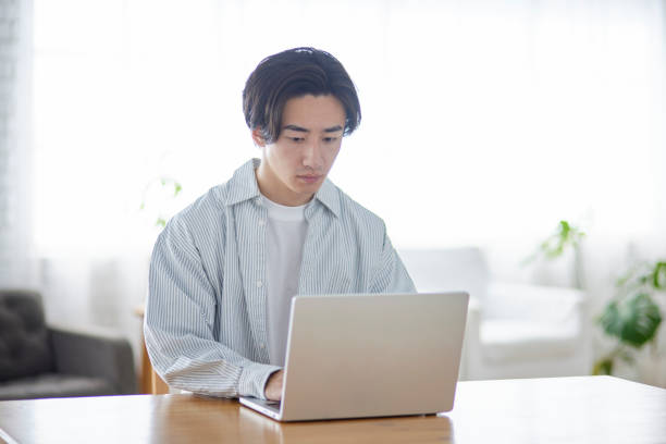 istock Male Japanese college student using a computer in the living room 2165054801