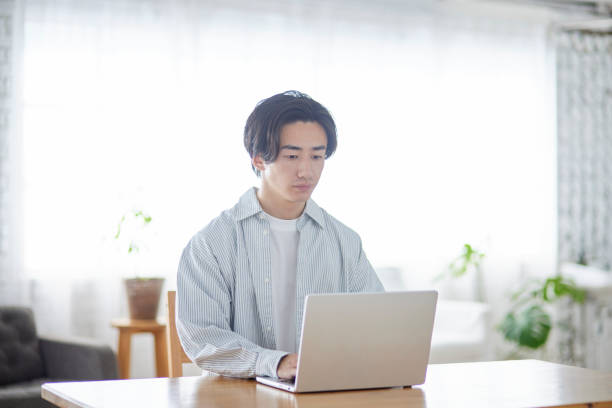 istock Male Japanese college student using a computer in the living room 2165054803