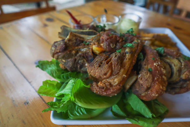 German pork knuckle is served with baked potatoes and sauce inside a white ceramic plate placed on the dining room table to make the pork knuckle ready for a dinner feast.