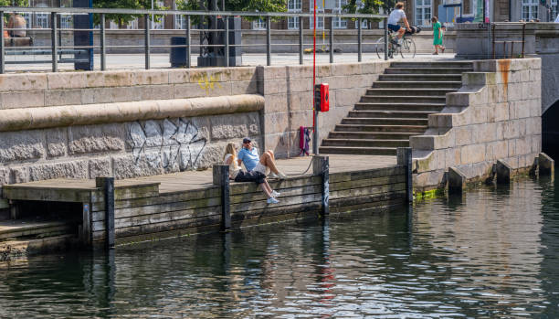 Copenhagen, Denmark  - August 2, 2024: Young people enjoying the sun by Frederiksholm Canal in central Copenhagen, Denmark