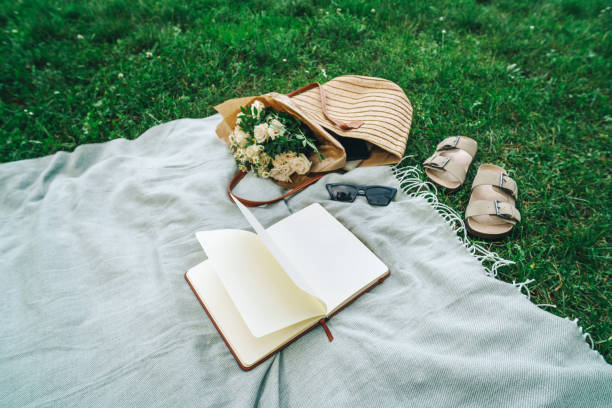 istock Solo picnic setup: straw bag, sandals, flowers and open journal in a park 2165061462