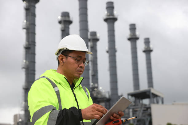 istock Senior power plant engineer with glow safety jacket and white hard hat working on a digital tablet and using walkie talkie  at the site power plant 2165061801