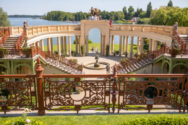 Schwerin, Mecklenburg-Western Pomerania - July 30, 2024: A panoramic view of the castle garden of Schwerin Castle with visitors and tourists on a sunny day with a blue, cloudless sky. The picture is symmetrically constructed. Stairs lead down from both sides into the garden, in the middle of which there is a beautiful fountain.