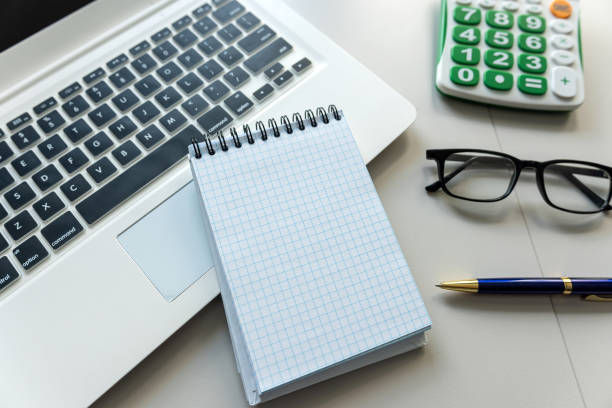 open notepad for notes with pen laptop and calculator on office white desk. Top view.