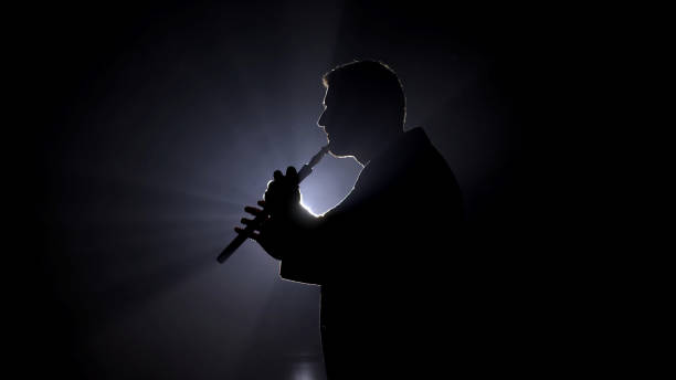silhueta de um homem com um chifre sob as luzes do palco. uma imagem marcante perfeita para promover apresentações ao vivo, eventos musicais e momentos dramáticos no palco. - shakuhachi - fotografias e filmes do acervo