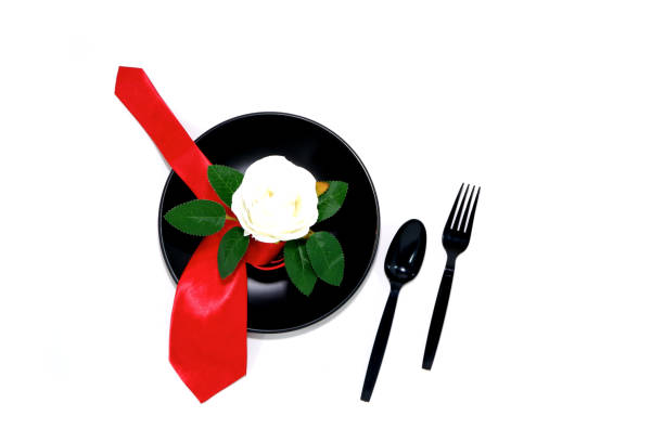 istock Black plate with fork and spoon with red tie isolated on white background close-up flat lay view 2165096237
