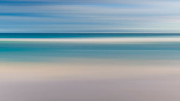 istock A blurry image of a beach with a blue ocean and white sand. The image has a dreamy, ethereal quality to it, as if it were a painting rather than a photograph. The water appears to be calm and still 2165130763