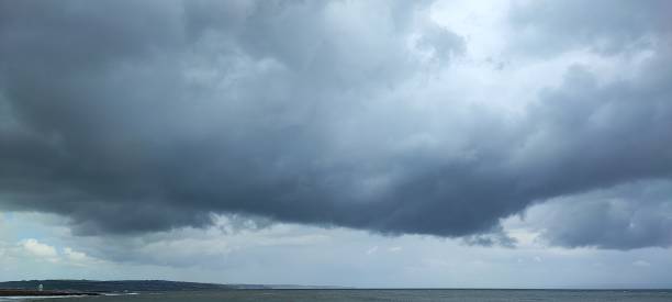 Moody dark clouds,  thunderstorms, thunder clouds over a beach at South Wales UK, Dark grey, sea, sand, beach, tourists, tourism.