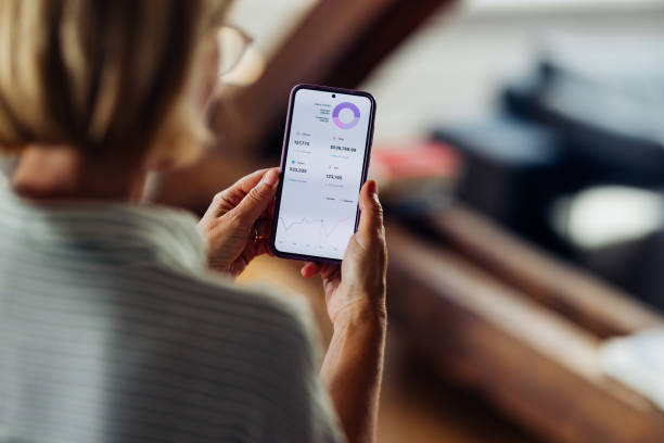 Woman Analyzing Financial Data on Smartphone at Home Close-up of a woman using a smartphone to review financial data and analytics at home, focusing on a detailed chart. looking at cell phone screen stock pictures, royalty-free photos & images