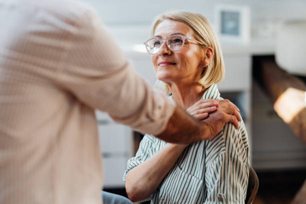 Senior Woman Supported by Male Friend in Modern Home Interior Senior woman being emotionally supported by a male friend indoors. The photo showcases warmth, care, and friendship in a modern home environment. personal care aid stock pictures, royalty-free photos & images