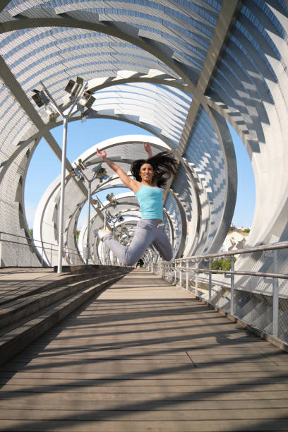 Young woman is jumping in the air on a modern bridge with her arms raised