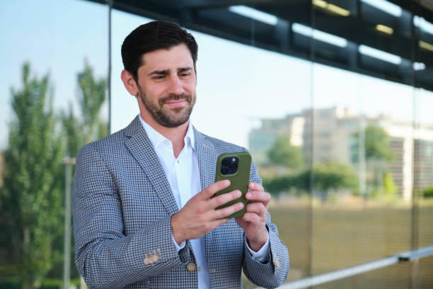 istock Businessman smiling and reading a text message on smartphone outside office building 2165145322
