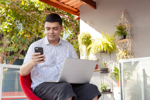 istock Man in a white shirt using a computer on a balcony with green space in the background. 2165145331