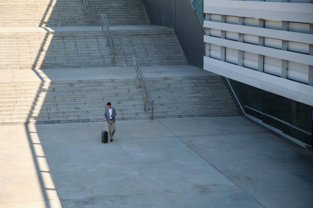 istock Businessman walking outside office building with rolling luggage and using smartphone 2165146730