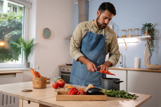 istock A man adds vegetables to a pot while preparing a home-cooked meal in a bright kitchen 2165148916