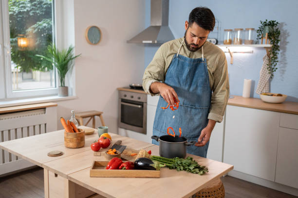 istock A man adds vegetables to a pot while preparing a home-cooked meal in a bright kitchen 2165148959