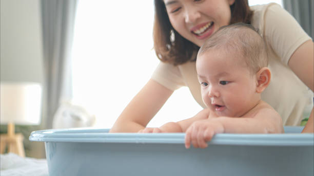 A tiny child enjoys taking a bath in a baby bathtub with mom