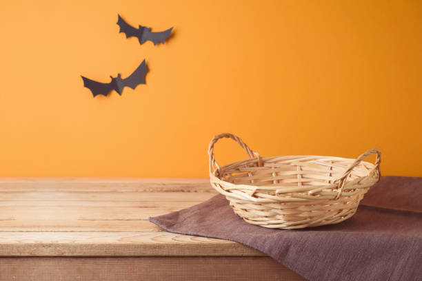 istock Empty basket with tablecloth on wooden table over orange wall and paper decorations background. Halloween mock up for design and product display. 2165167593