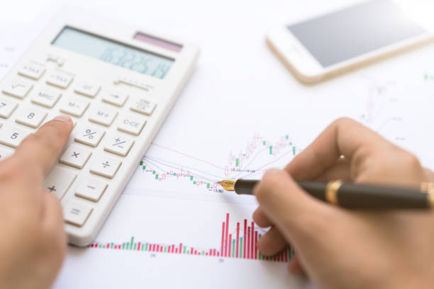 istock Calculator, magnifying glass, coin, and pen placed on the candlestick chart 2165174656