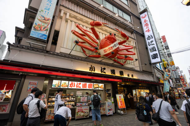 Osaka, Japan - June 17, 2024 : People walk through the Dotonbori district of Osaka, Japan. Kani Doraku crab restaurant put a giant crab billboard at its entrance.