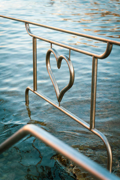 Heart-shaped metal railing over calm water with gentle waves, symbolizing love and tranquility in a serene setting.