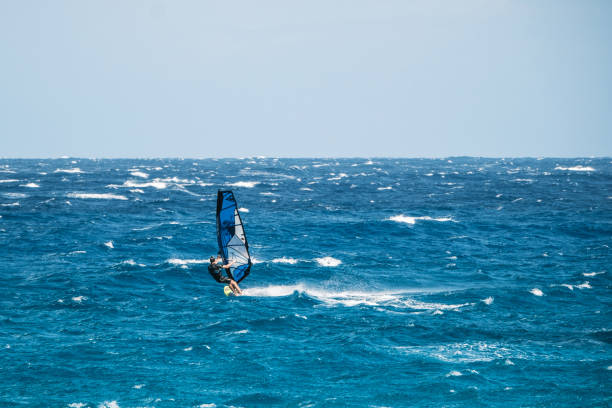 A sailboat is sailing in the ocean. The sail is yellow and green. The sky is clear and the water is calm