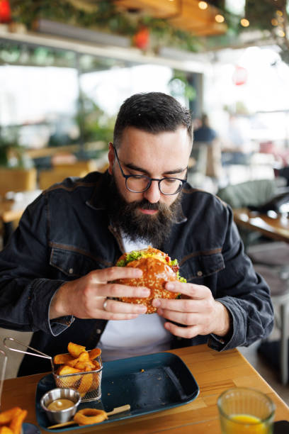 istock Young man having burger for lunch in fast food restaurant 2165198934