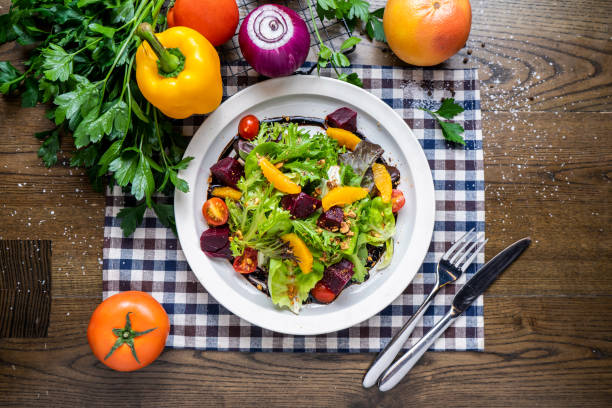 istock Roasted Beetroots Salad with orange, cherry tomato, spinach, tomato, onion, capsicum, coriander, knife and fork served in dish isolated on napkin top view of italian fastfood on wooden table 2165206240