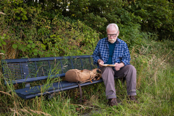 istock Mature man sitting on a bench reading a book 2165208881