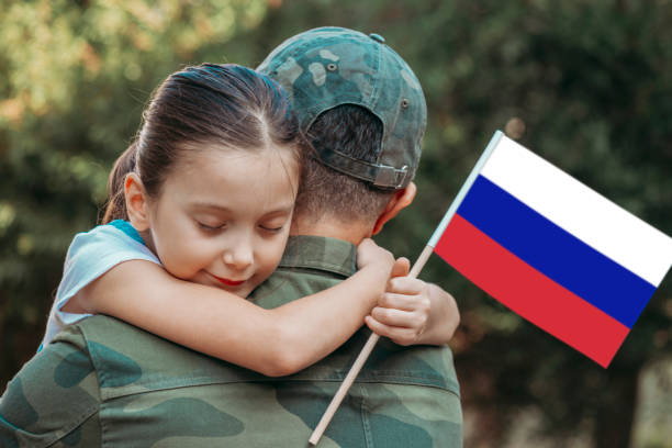 Little girl hugs the soldier father and holding Russian Flag.
