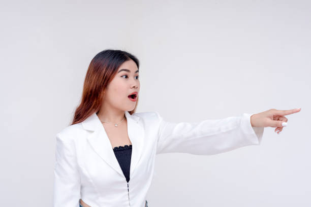istock A shocked young woman with raised eyebrows and mouth wide open facing sideways while pointing to the right. Isolated on a white background. 2165215234