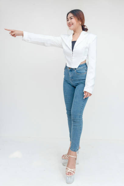 A cheerful young woman pointing and looking to the left while smiling. Isolated on a white background.
