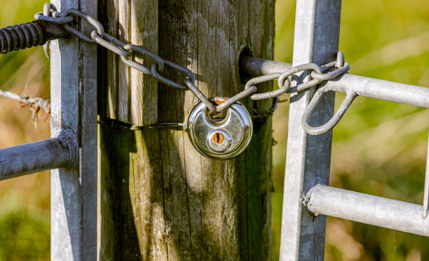 istock wooden post, silver padlock and linked chain outside in the sun 2165218463