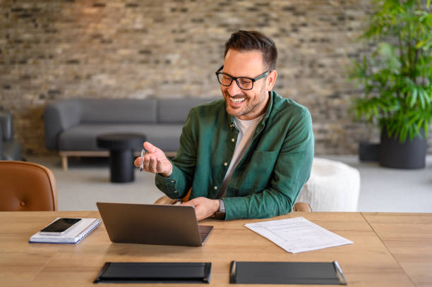 istock Male computer programmer smiling and discussing project details over video call on laptop in office 2165225072