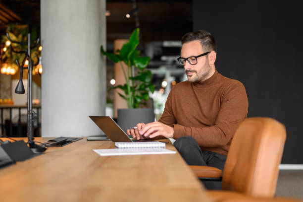istock Focused male programmer in eyeglasses working serious on project over computer at desk in office 2165225115