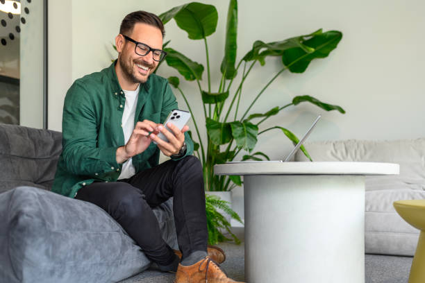 istock Full length of freelancer using applications over mobile phone while sitting on sofa in modern office 2165225161