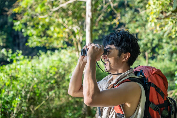 istock Young Asian man hiker using binoculars to explore forest and enjoy the wilderness on outdoor adventure. Bird watching. 2165227556