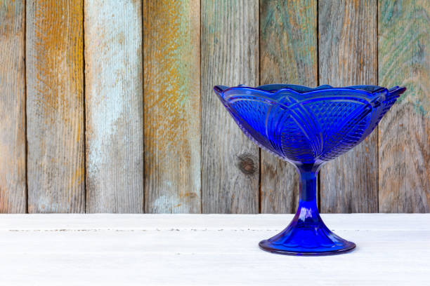 blue glass vintage empty fruit bowl on a white table on a wooden wall background with a copy space