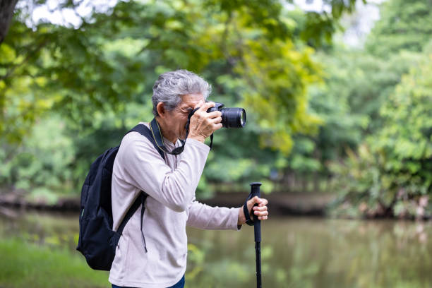 istock Asian senior man is trekking in the forest while using camera to take memorable photo for elder exercise outdoor and nature environment therapy concept 2165244526