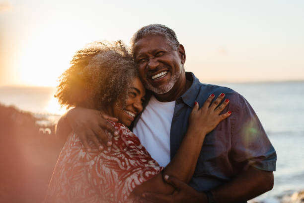 Elderly pair embracing at sunset, sharing joy and love by the seaside Elderly pair embraces at sunset, radiating joy and love by the seaside. A beautiful moment of togetherness and happiness. black couple sunset stock pictures, royalty-free photos & images