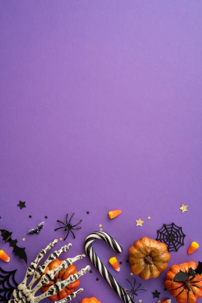 istock Halloween vertical themed background featuring spooky decorations, candy, and pumpkins on a purple surface 2165250002