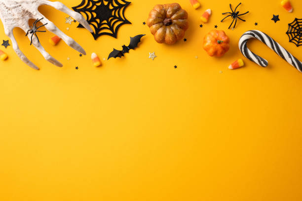 istock Halloween background with spooky decorations including pumpkins, candy corn, spiders, bats, and cobwebs on a yellow backdrop 2165250010