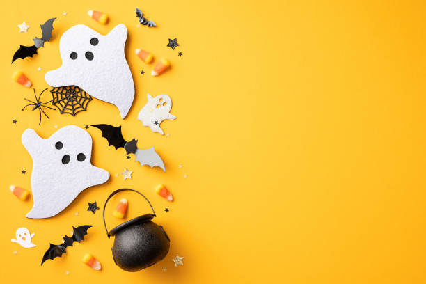 istock Festive Halloween arrangement featuring ghosts, bats, candy corn, and a cauldron on a yellow background 2165250016